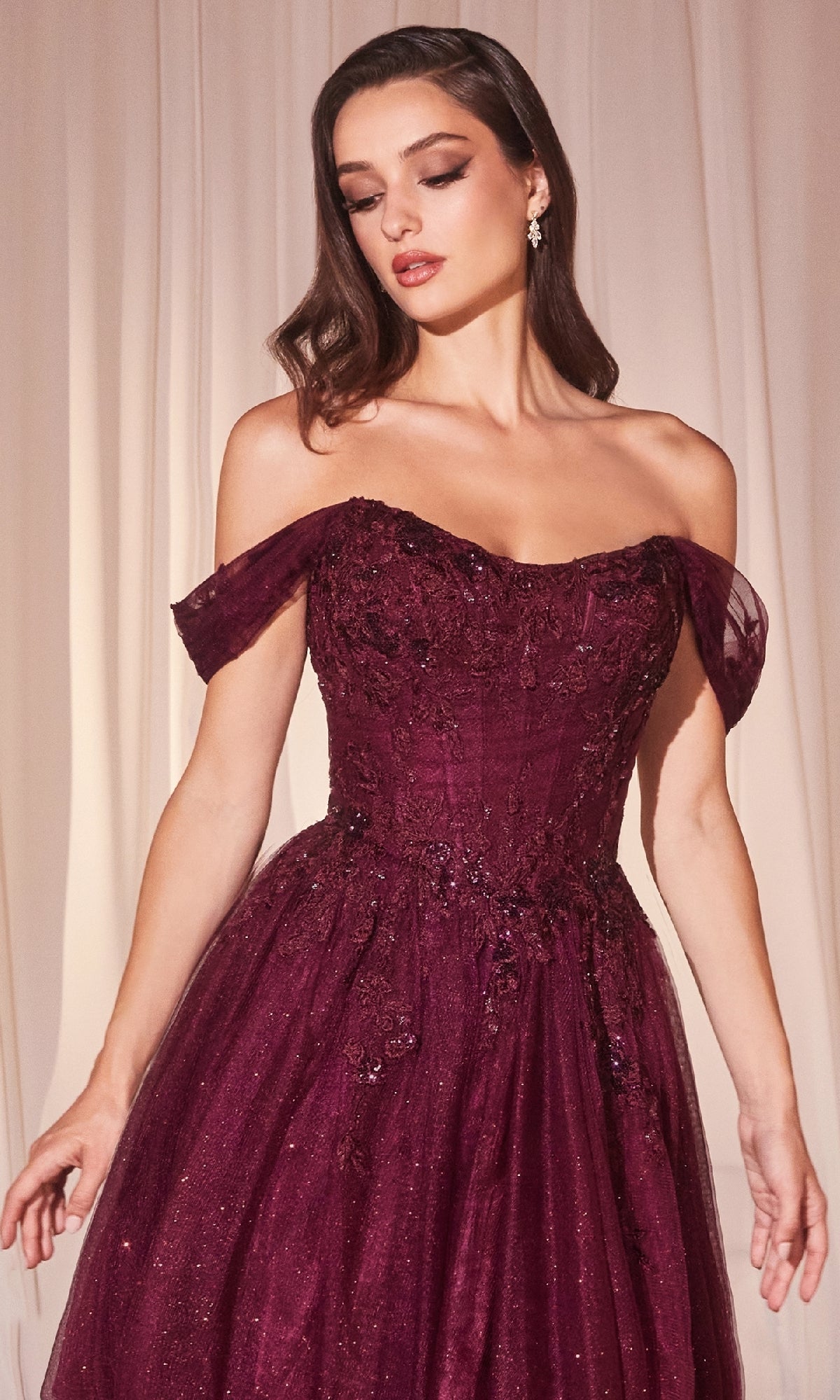 A woman models the Ladivine CD799 Off-Shoulder Long Prom Dress in deep burgundy, featuring intricate detailing. Perfect as an elegant evening gown for special occasions, shown against light-colored draped curtains.